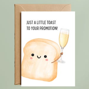 May include: Greeting card with a cartoon slice of bread holding a champagne glass. The card reads "JUST A LITTLE TOAST TO YOUR PROMOTION!" The card is white with a brown envelope.