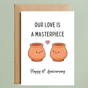 May include: A white greeting card with the text "OUR LOVE IS A MASTERPIECE" and "Happy 9th Anniversary". The card features two cartoon pots with smiling faces and a small pink heart. The card is inside a brown envelope.