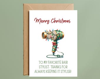 May include: A white greeting card with a brown envelope featuring a green hair dryer wrapped in colorful Christmas lights and a red bow. The text reads Merry Christmas TO MY FAVORITE HAIR STYLIST. THANKS FOR ALWAYS KEEPING IT STYLISH!