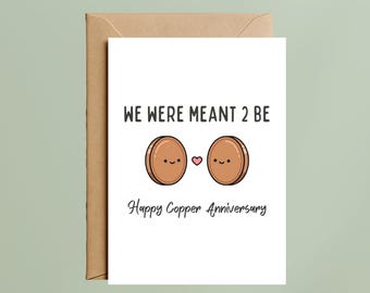 May include: A white greeting card with the text "WE WERE MEANT 2 BE" and "Happy Copper Anniversary". The card features two cartoon coins with smiling faces and a pink heart between them. The card is inside a brown envelope.