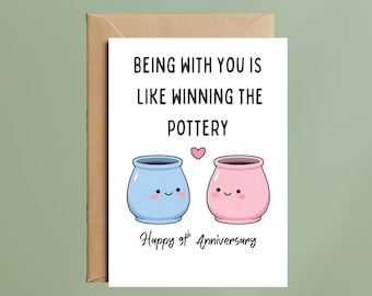May include: A white greeting card with a brown envelope featuring the text Being with you is like winning the pottery, a small pink heart, two smiling pots in light blue and pink, and the text Happy 9th Anniversary at the bottom.