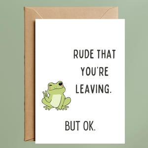 May include: A white greeting card with the text "RUDE THAT YOU'RE LEAVING. BUT OK." features a cartoon frog giving a peace sign. The card is inside a brown envelope, set against a light green background.