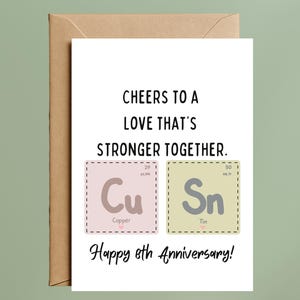 May include: A white greeting card with the text "CHEERS TO A LOVE THAT'S STRONGER TOGETHER." Features the chemical symbols Cu and Sn, representing copper and tin. The card is for an 8th anniversary and is inside a brown envelope.