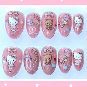 Könnte beinhalten: Ein Set aus zehn mandelförmigen Press-on-Nägeln mit einer rosa Glitzerbasis. Die Designs zeigen Hello Kitty-Figuren, braune Teddybären, rosa Schleifen, Herzformen und das Wort Love, akzentuiert mit kleinen klaren Strasssteinen und sternförmigen Edelsteinen.