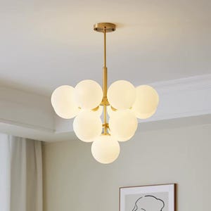 Peut inclure: Un lustre doré avec huit globes en verre blanc givré. Le lustre a un design simple avec une tige centrale et les globes sont disposés en grappe autour de celle-ci.