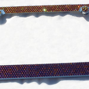May include: A silver license plate frame with a border of iridescent purple and gold rhinestones.