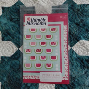 May include: A package for a quilt pattern titled "Watermelon Patchwork" by Thimble Blossoms. The pattern features a design of watermelon slices in shades of pink, red, and green on a light blue background. The package is in a clear plastic sleeve.
