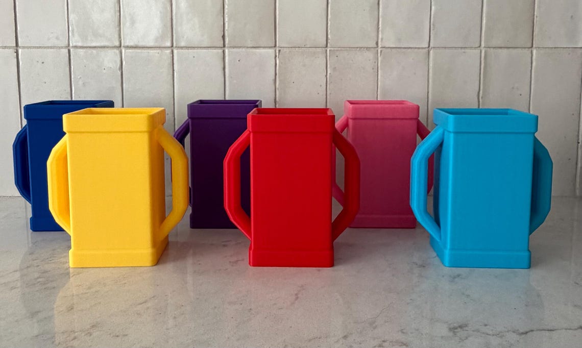 Six juice box holders in a row on a marble counter, in dark blue, yellow, purple, red, pink and light blue.