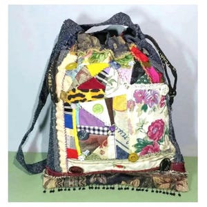 Könnte beinhalten: Eine Patchwork-Tragetasche mit einem Denim-Trageriemen und einem Kordelverschluss. Die Tasche ist aus verschiedenen Stoffen gefertigt, darunter Blumenmuster, Karo und Tiermuster. Die Tasche hat einen Fransenbesatz und schwarze Perlen am Boden.