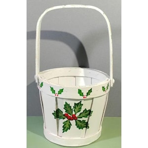 Puede incluir: Cesta de madera blanca con asa, decorada con hojas de acebo verdes y bayas rojas.