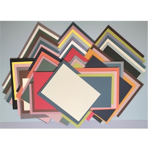 May include: A collection of colorful, layered paper mats in various sizes and hues, including white, red, blue, and green. The mats are arranged in a visually appealing, overlapping pattern against a light blue background, suitable for framing artwork or photographs.