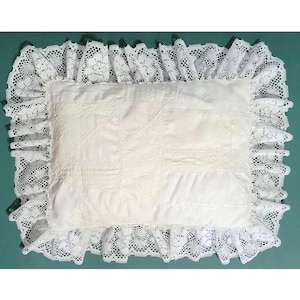 May include: White pillow with a lace trim. The pillow is made of a patchwork of white fabric squares.
