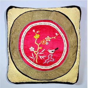 Peut inclure: Un coussin carré avec une bordure dorée et noire. Le centre du coussin présente un cercle rouge avec un oiseau blanc et un motif floral brodé.