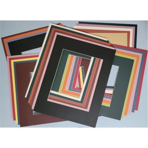 May include: A collection of colorful picture mats in various sizes and colors, including black, brown, green, and blue. The mats are arranged in a layered display, showcasing a range of hues and styles for framing artwork or photographs.