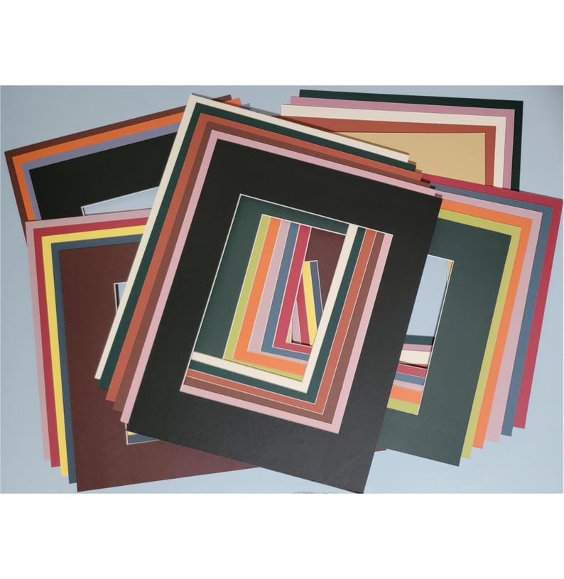 May include: A collection of colorful picture mats in various sizes and colors, including black, brown, green, and blue. The mats are arranged in a layered display, showcasing a range of hues and styles for framing artwork or photographs.