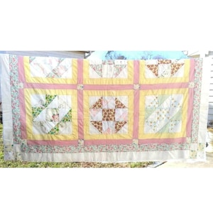 May include: A vintage quilt with a patchwork design featuring a variety of floral and geometric patterns in shades of pink, yellow, and white.