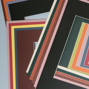 May include: A stack of colorful picture mats in various sizes and colors. The mats include black, brown, green, pink, orange, and yellow. The mats are layered on top of each other, creating a visually appealing display.