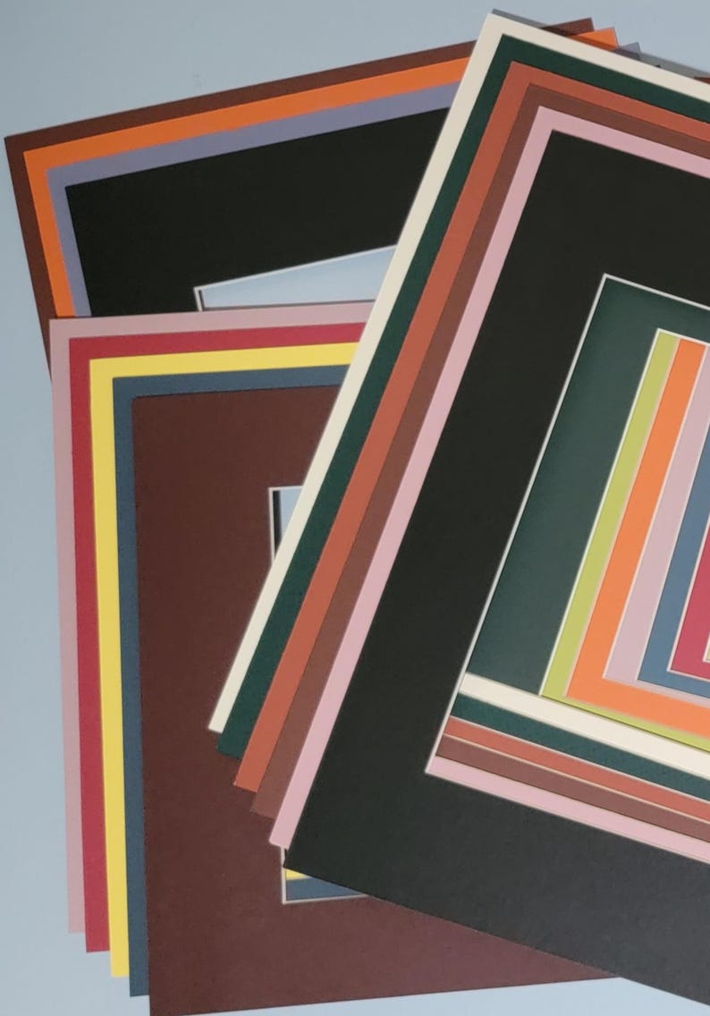 May include: A stack of colorful picture mats in various sizes and colors. The mats include black, brown, green, pink, orange, and yellow. The mats are layered on top of each other, creating a visually appealing display.