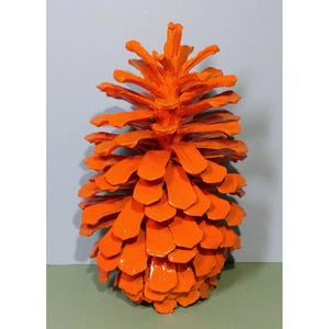 Può includere: Un grande pigna arancione con una finitura lucida. La pigna è realizzata in legno naturale ed è stata dipinta di un colore arancione brillante.