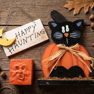 Set di Halloween da 3 pezzi composto da un gattino nero intagliato a mano e dipinto su una mensola, vestito da zucca, un portacandele e un cartello con la scritta "Happy Haunting".