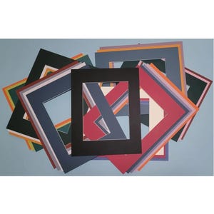 May include: A collection of colorful picture frame mats in various sizes and shapes, including square and rectangular. The mats are in shades of blue, red, black, green, and orange, with white and gray accents. The mats are arranged on a light blue surface.