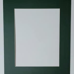 May include: A white picture frame mat with a dark green border and a rectangular opening. The mat is set against a white background, creating a clean and simple aesthetic. Ideal for showcasing photographs or artwork.