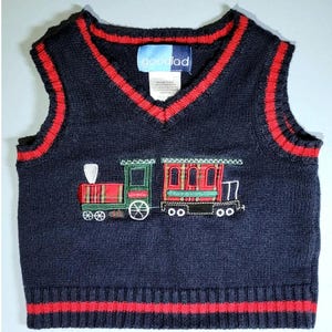 May include: A navy blue knitted vest with red trim and an embroidered train design. The vest has a V-neck and the brand name "goodlad" is visible on the label.
