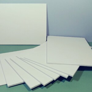 May include: A collection of white foam boards of varying sizes, arranged on a teal surface against a light blue backdrop. The boards are rectangular and appear to be unused, with clean, smooth surfaces. The arrangement suggests a crafting or art supply theme.
