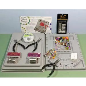 May include: A gray beading design board with a clear plastic bag of colorful beads, a spool of wire, and two pairs of pliers. The board has a circular design area and a ruler on the side. The text "Bead Design Board" is printed on the board.