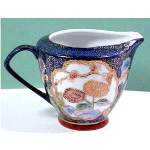 May include: A small, blue and white porcelain creamer with a floral design. The creamer has a gold rim and a red base.