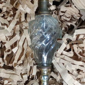 May include: A clear glass table lamp with a gold metal base and a twist design. The lamp has a cord and a switch on the side.