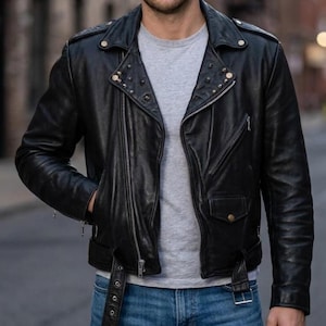 May include: A black leather motorcycle jacket featuring a wide notched collar with silver-toned metal studs, an asymmetrical front zipper closure, a diagonal zippered chest pocket, a small flap pocket with a snap button, and an adjustable waist belt.