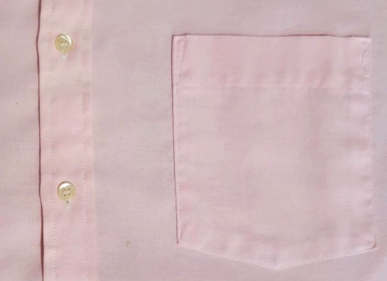 K&ouml;nnte beinhalten: Ein rosa Hemd mit Kn&ouml;pfen und einer einzigen Brusttasche.
