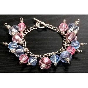 May include: A silver charm bracelet with a toggle clasp and pink and blue faceted glass beads.