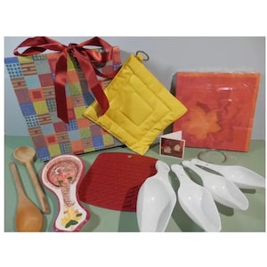 Pode incluir: Uma coleção de artigos para casa e cozinha, incluindo uma sacola de presente colorida com uma fita vermelha, um pegador de panela acolchoado amarelo, um descanso de panela de silicone vermelho, colheres de pau e conchas brancas. Há também uma peça decorativa de cerâmica e um cartão de felicitações.
