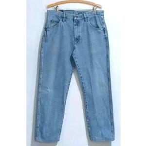 Może przedstawiać: Jasne niebieskie dżinsy z prostymi nogawkami. Dżinsy mają klasyczny krój z pięcioma kieszeniami i zapięciem na guziki.