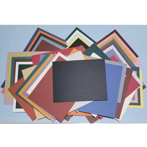 Op de afbeelding: Een grote collectie rechthoekige vellen karton in een grote verscheidenheid aan kleuren, waaronder zwart, blauw, rood, groen, geel, roze en bruin. De vellen zijn gelaagd en waaiervormig neergelegd, met verschillende tinten en kleuren.