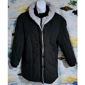 May include: A black quilted jacket with a white trim and a white lining. The jacket has a button closure and a stand-up collar.