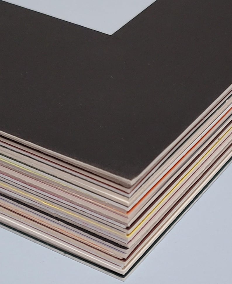 May include: A stack of black and white photo mats with various colored edges. The mats are stacked on top of each other, with the top mat being black and the bottom mats showing a variety of colors.
