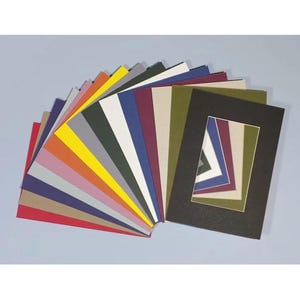Op de afbeelding: Een waaier van gekleurde passe-partouts, met een verscheidenheid aan tinten, waaronder rood, oranje, geel, groen en blauw. Een zwart passe-partout met een gelaagd, geometrisch ontwerp is ook aanwezig, wat een contrast biedt.