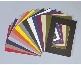 Può includere: Una collezione di passe-partout colorati a ventaglio, che mostra una varietà di tonalità tra cui rosso, arancione, giallo, verde e blu. È presente anche un passe-partout nero con un design geometrico a strati, che offre un contrasto.