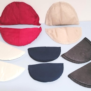 Puede incluir: Surtido de hombreras en varios colores, incluyendo rojo, beige, blanco, azul marino y gris. Las hombreras son semicirculares y parecen ser de tela. Ideales para alteraciones de ropa o proyectos de manualidades.