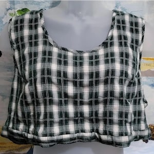 Pode incluir: Um top curto sem mangas com padrão xadrez preto e branco. O top tem um decote redondo e um caimento solto.