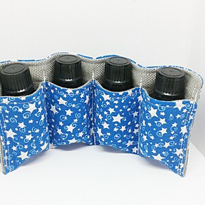 May include: A blue fabric essential oil bottle holder with a white star and swirl pattern. The holder has four pockets, each holding a black bottle. The interior lining is gray.