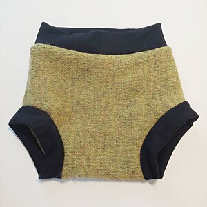 Puede incluir: Un par de bragas de bebé con un cuerpo de tela texturizada verde oliva y ribete acanalado azul marino en la cintura y las aberturas de las piernas. Las bragas están diseñadas para la comodidad y el estilo.