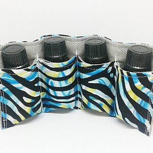 May include: A fabric essential oil bottle holder with four compartments. The holder features a zebra print design in blue, black, and yellow. The interior is a light gray fabric. Each compartment holds a black bottle with a black cap.