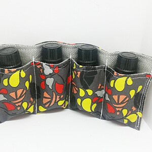 May include: A fabric essential oil bottle holder with four pockets. The holder is gray with a colorful floral pattern in yellow, red, and orange. Each pocket holds a black-capped bottle.