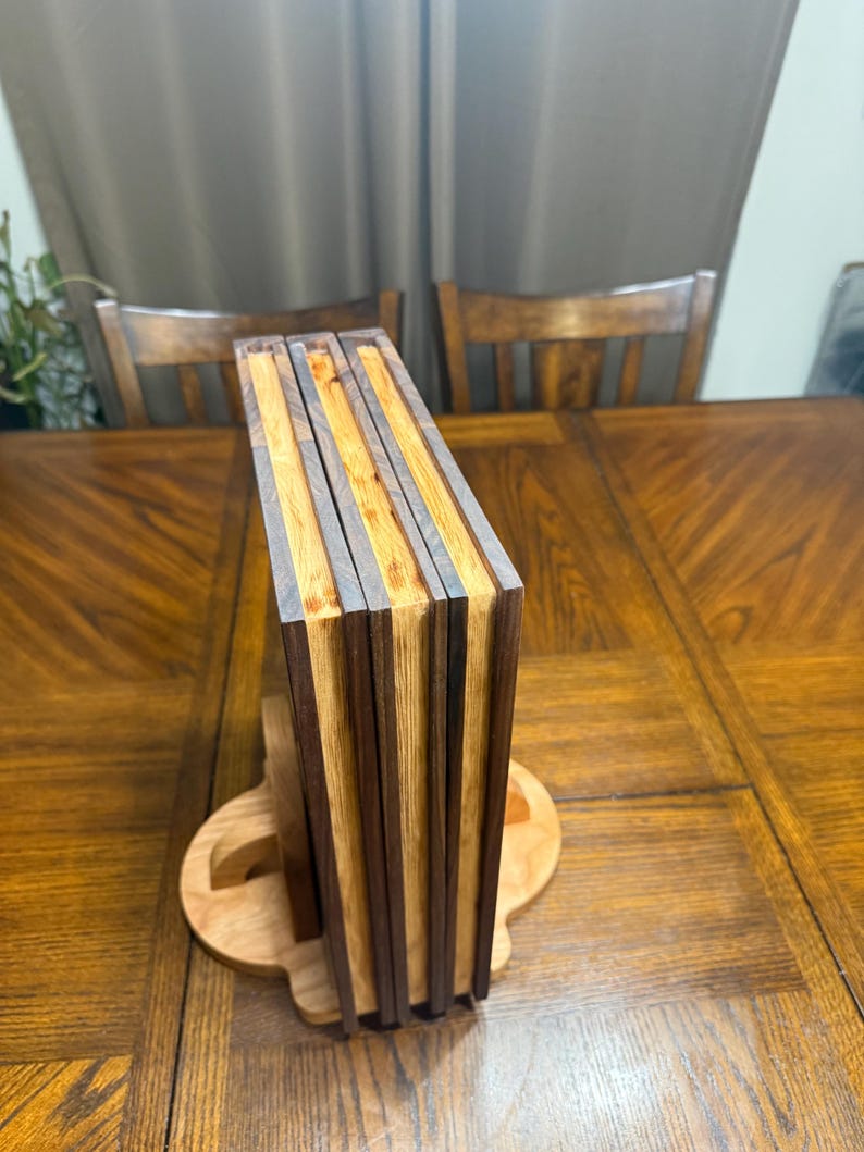 May include: A wooden book stand with a stack of books. The books have alternating dark and light wood stripes. The stand is made of light-colored wood and is on a wooden table.