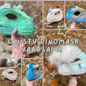 May include: A collage of dinosaur masks in various colors, including green, blue, and white. The masks are handmade and have a textured, crusty appearance. Text on the image reads "CRUSTY DINOMASK YARDSALE!"