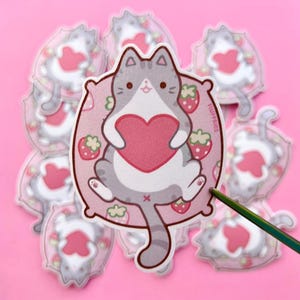 chat tigré gris étreignant le coeur scintillant autocollant givré | Vinyle imperméable | Papeterie kawaii mignonne